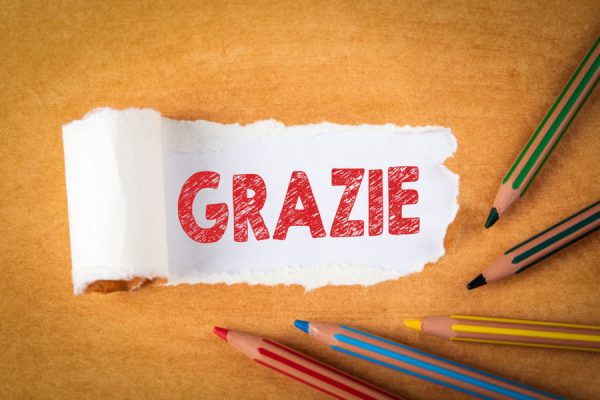 Word Grazie Means Thank You. Colored pencils on an orange background Word Grazie Means Thank You. Colored pencils on an orange background. Text under torn paper